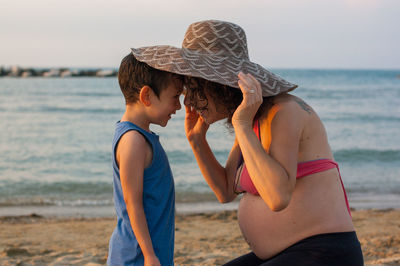 Smiling pregnant mother and son against sea at beach