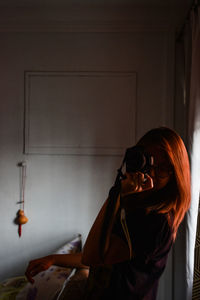 Side view of young woman standing against wall at home