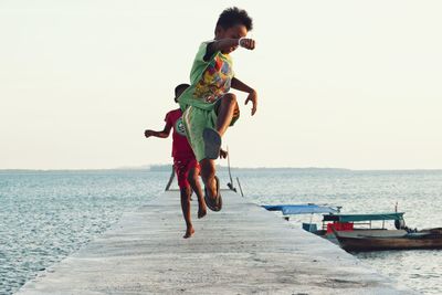 Boys jumping on pier at beach against sky