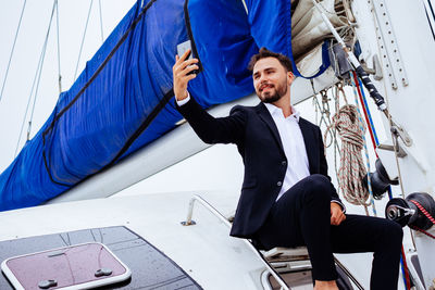 Young man sitting on boat against blue sky