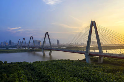 Suspension bridge over river against cloudy sky