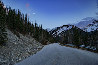 Road amidst snowcapped mountains against night sky with full moon