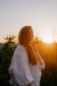 Rear view of woman standing against sky during sunset