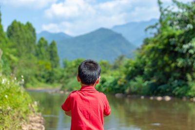 Rear view of boy looking at lake against mountain