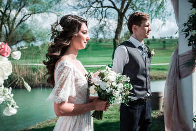 Young couple holding flower bouquet against plants