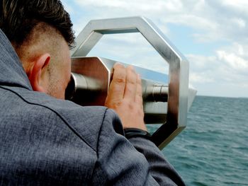 Close-up of man looking through coin-operated binoculars against sea