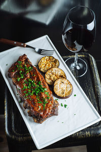 Top view of delicious grilled pork ribs garnished with fresh parsley served with sliced grilled eggplant on white tray