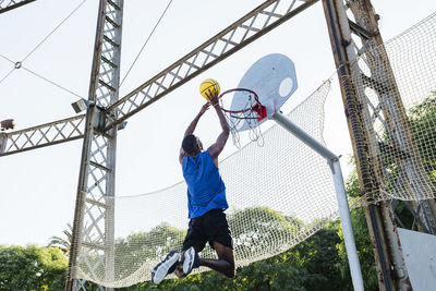 Young man dunking basketball while playing at sports court