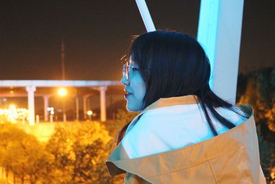 Portrait of young woman looking at illuminated building at night