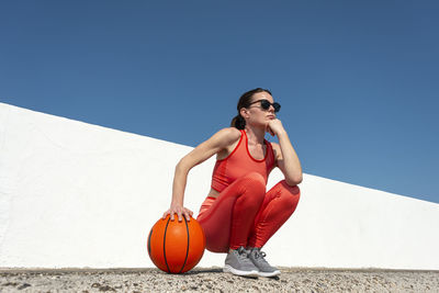 Female basketball player, crouching holding a basketball, outside in the sun.