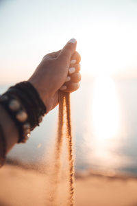 Midsection of person holding sand against sky during sunset