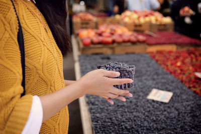 Midsection of woman holding blueberries at market stall