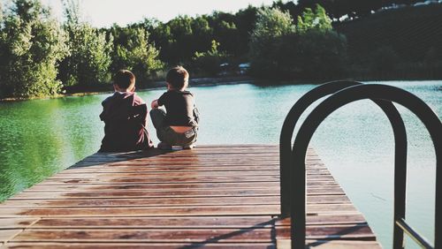 Rear view of siblings on pier over lake