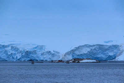 Scenic view of sea by snowcapped mountain against sky