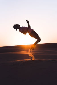 Silhouette man skateboarding on beach against clear sky during sunset