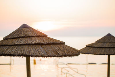 Thatched parasols at beach against sky during sunset