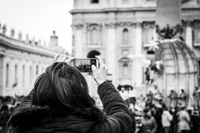 Rear view of woman photographing building in city