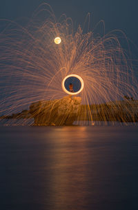 Man spinning wire wool over sea on rock at night