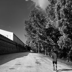 Rear view of man jogging on road by trees against sky