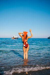 Rear view of woman jumping in sea against clear blue sky