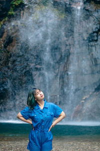 Young woman standing against waterfall