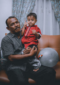 Portrait of man with son sitting on sofa at home