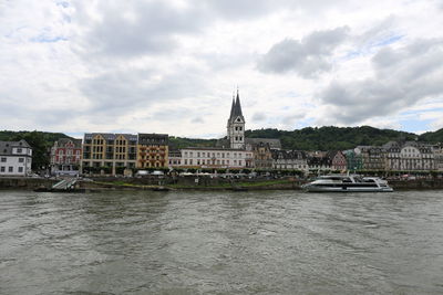 View of buildings by river against cloudy sky