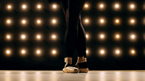 Low section of female ballet dancer standing on stage floor against illuminated lights