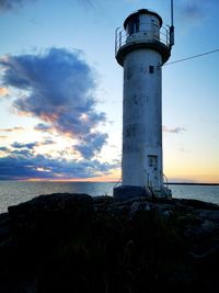 Lighthouse by sea against sky during sunset