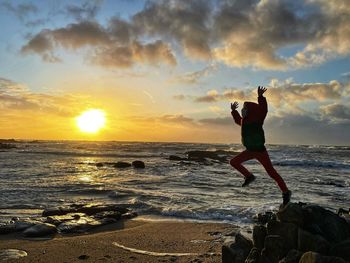 Man standing on rock at beach against sky during sunset