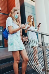 Young women girls spending time together downtown using smartphones social media sending texts