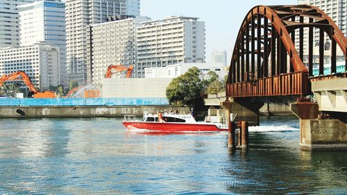 Boat moving in river under bridge by city