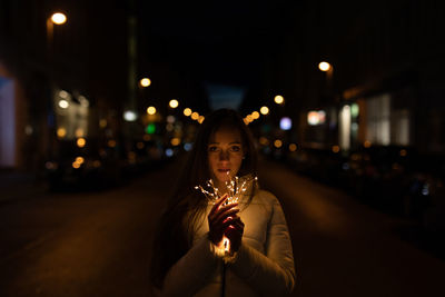 Portrait of woman standing on illuminated street at night