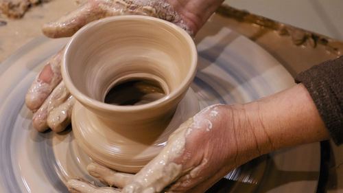 Cropped hands of craftsperson making clay product in pottery workshop