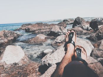 Low section of person on rock at beach against clear sky