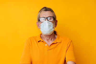 Portrait of young woman wearing mask against yellow background