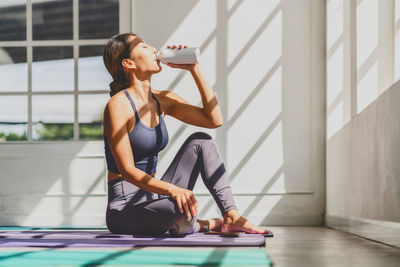 Asian woman drinking after practicing yoga at home on the yoga mats,exercises at home concept