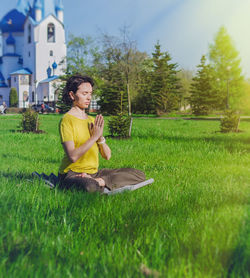 Woman sitting in prayer position while meditating on grassy field at park