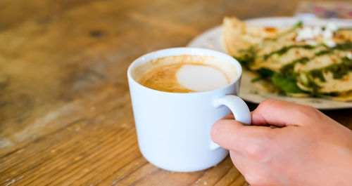 Cropped image of hand holding coffee cup on table