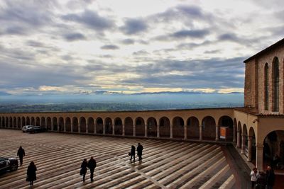 Group of people in front of historical building against cloudy sky