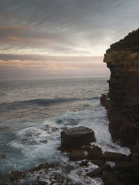 Scenic view of sea and cliffs against sky during sunset