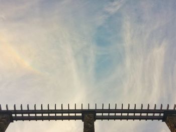 Low angle view of structure against cloudy sky with rainbow