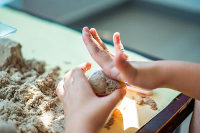Cropped hand of child playing with sand on table