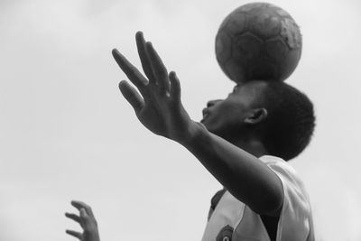 Low angle view of boy balancing soccer ball against clear sky