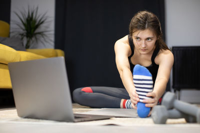 Young woman exercising while watching video on laptop