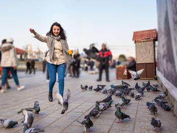 Full length of smiling woman feeding pigeons