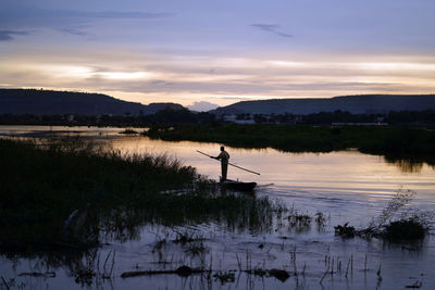 Silhouette man standing by lake against sky during sunset
