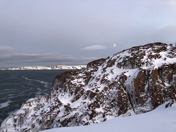 Scenic view of sea by snowcapped mountain against sky