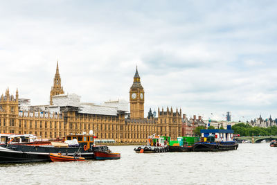 Boats in thames river by palace of westminster and big ben against sky