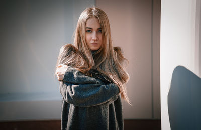 Portrait of a young woman standing against wall at home